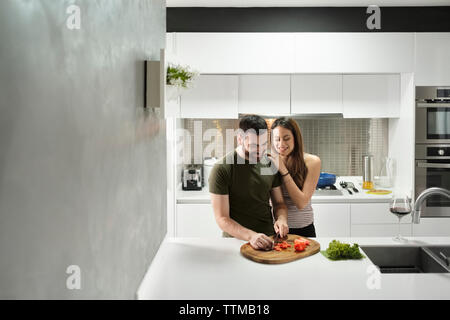 Il ragazzo sorridente Tritare i pomodori in cucina con amorosa ragazza in casa in affitto Foto Stock