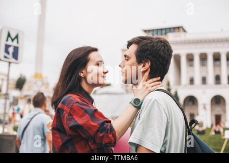 Vista laterale della giovane coppia in cerca di ogni altra faccia a faccia in città Foto Stock