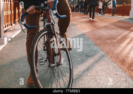 Sezione bassa del ciclista equitazione Bicicletta sul ponte in città durante il tramonto Foto Stock