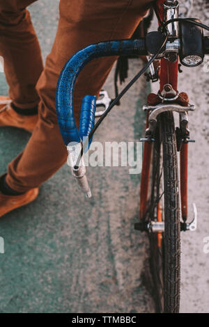 Sezione bassa del ciclista maschio con noleggio biciclette in piedi sul ponte in città durante il tramonto Foto Stock