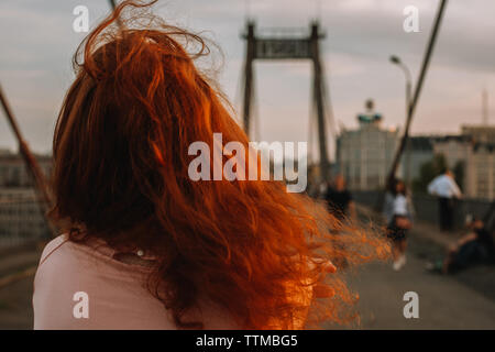 Vista posteriore di una donna con i capelli rossi camminando sul ponte in città Foto Stock