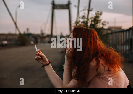 Giovane donna redhead sigaretta di contenimento nella parte anteriore del suo viso Foto Stock