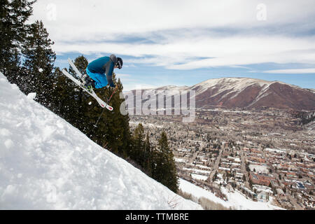 Stati Uniti d'America, Colorado, Aspen, sciatore prendere l'aria su un sentiero denominato cavatappi con la città di Aspen in distanza, Aspen Ski Resort, monte Ajax Foto Stock