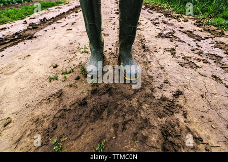 Sporco del contadino Stivali in gomma su terreni fangosi country road. Agronomo è a piedi il percorso attraverso campi coltivati dopo una forte tempesta di pioggia. Foto Stock