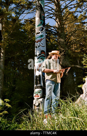 Stati Uniti d'America, Alaska, Sitka, Tommy Giuseppe un Tinglit totem pole carver si erge di fronte a uno dei suoi intagli, Halibut Cove, Sitka Sound Foto Stock