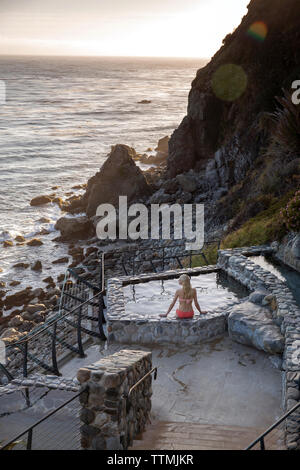 Stati Uniti, California, Big Sur, Esalen, una donna si siede sul bordo della primavera calda ai bagni e prende la sera vista il Esalen Institute Foto Stock