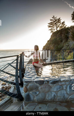Stati Uniti, California, Big Sur, Esalen, una donna si siede presso le Terme e si affaccia sul Big Sur costa al tramonto, il Esalen Institute Foto Stock