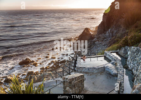 Stati Uniti, California, Big Sur, Esalen, una donna si siede sul bordo della primavera calda ai bagni e prende la sera vista il Esalen Institute Foto Stock