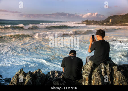 HAWAII, Oahu, North Shore spettatori guardando il grande si gonfiano le onde in rotolamento sulla sponda nord Foto Stock