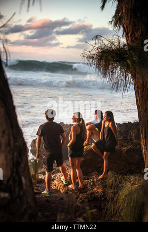 HAWAII, Oahu, North Shore, astanti guardare un grande rigonfiamento in rotolo al tramonto a Pupukea Beach Park sulla sponda nord Foto Stock