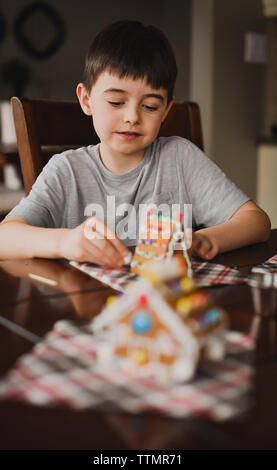 Giovane ragazzo caramelle mettendo su una casa di panpepato. Foto Stock