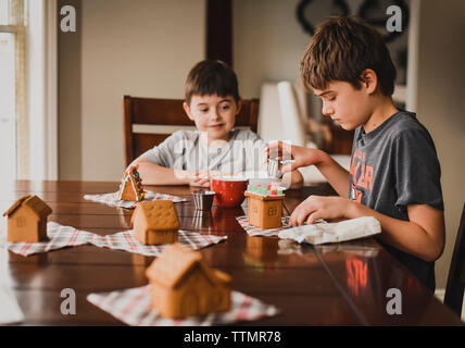 Due ragazzi decorare Gingerbread case insieme al tavolo. Foto Stock