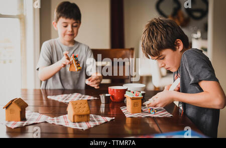 Due ragazzi decorare Gingerbread case insieme al tavolo. Foto Stock