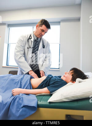 Medico esaminando l'addome del bambino su un tavolo di esame di una clinica. Foto Stock