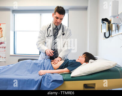 Medico esaminando l'addome del bambino su un tavolo di esame di una clinica. Foto Stock