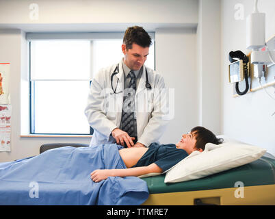 Medico esaminando l'addome del bambino su un tavolo di esame di una clinica. Foto Stock