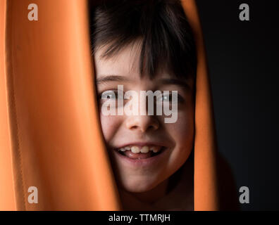 Ritratto di un giovane ragazzo felice peeking la sua testa attraverso le tende. Foto Stock