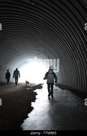 La famiglia e il loro cane a piedi attraverso un gelido tunnel metallico in inverno. Foto Stock