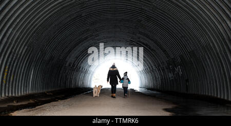 Madre e figlio e cane a piedi attraverso un tunnel metallico su un giorno d'inverno. Foto Stock