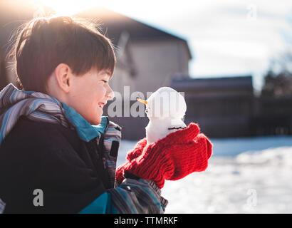 Giovane ragazzo sorridente in un minuscolo pupazzo di neve che egli tiene nelle sue mani. Foto Stock