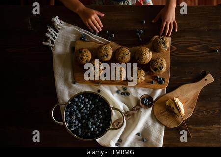 Tagliate le mani della ragazza con i cookie e i mirtilli sul tavolo di legno a casa Foto Stock