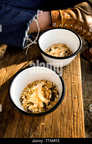 Sezione bassa della giovane donna con cereali da prima colazione in ciotole sul tavolo di legno Foto Stock