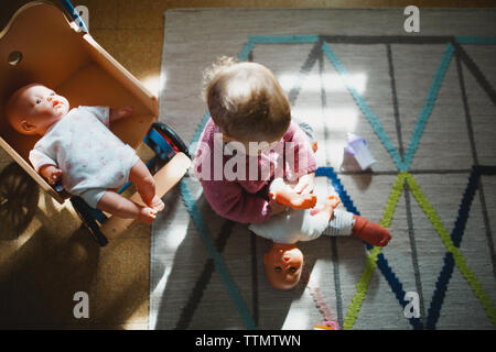 Una bambina seduta sul tappeto a giocare con le sue bambole Foto Stock