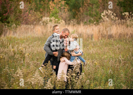 Genitori felici che abbraccia i bambini mentre in piedi in mezzo a piante contro gli alberi nelle foreste Foto Stock