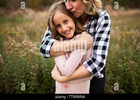 Felice madre abbracciando la figlia mentre in piedi in mezzo a piante in foresta Foto Stock