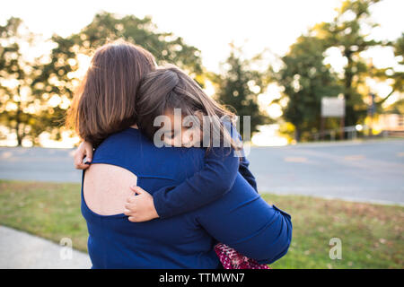 Vista posteriore della madre che porta la figlia a pelo mentre in piedi contro il cielo in posizione di parcheggio Foto Stock