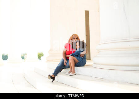Ritratto della figlia abbracciando la madre mentre è seduto sui gradini contro le colonne Foto Stock