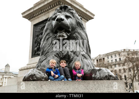 Tre Fratelli sorridente sedersi sulla Trafalgar Square Lion Foto Stock