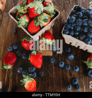 Angolo di alta vista di mirtilli e fragole in scatole sul tavolo di legno Foto Stock