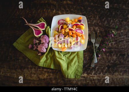 Alta vista angolare di insalata servita nella piastra con i fiori e le forcelle da igienico sul tavolo di legno Foto Stock