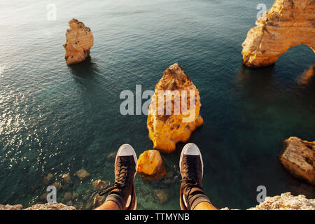 Sezione bassa dell'uomo indossando scarpe in appoggio sulla scogliera contro il mare Foto Stock