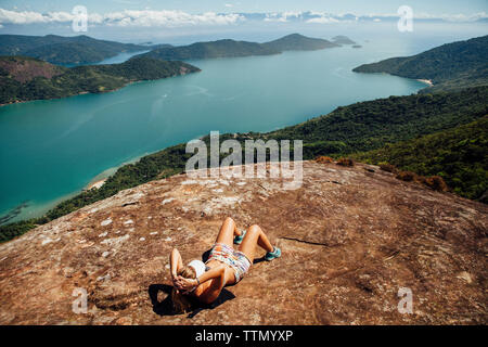 Elevato angolo di visione della donna rilassante sulla montagna in mare durante la giornata di sole Foto Stock