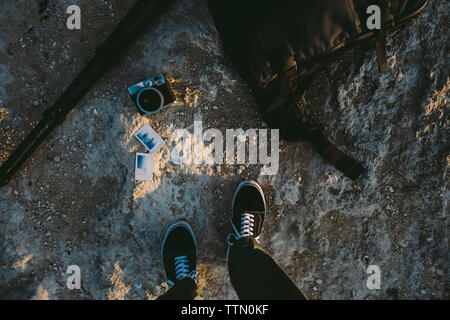 Sezione bassa dell uomo in piedi dalla fotocamera e foto istantanea sulla formazione di roccia presso la spiaggia durante il tramonto Foto Stock