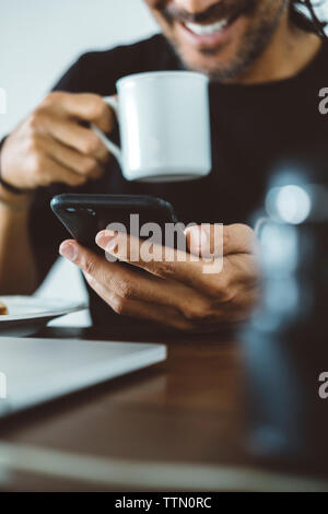 Sezione mediana dell'uomo un caffè mentre si utilizza il telefono cellulare a casa Foto Stock