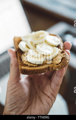 Ritagliate la mano dell'uomo azienda con pane e fette di banana a casa Foto Stock