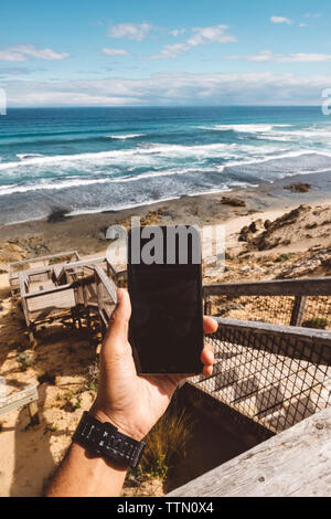 Ritagliate la mano di un escursionista azienda smart phone contro il mare Foto Stock
