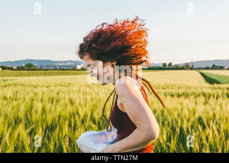 Vista laterale della donna in esecuzione presso l'azienda contro il cielo chiaro durante il tramonto Foto Stock