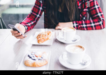 Sezione mediana della donna con la colazione a tavola utilizzando il telefono cellulare in cafe Foto Stock