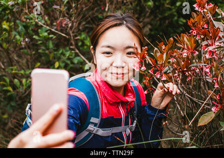 Close-up di escursionista femmina tenendo selfie con piante in foresta Foto Stock