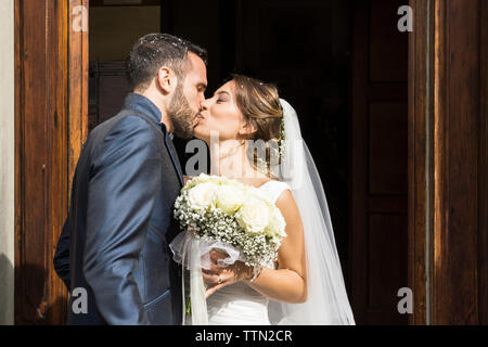 Sposa giovane kissing mentre in piedi all ingresso della chiesa Foto Stock