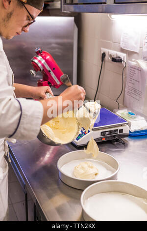 Voce maschile baker versando l'impasto nelle teglie sul bancone cucina in laboratorio Foto Stock