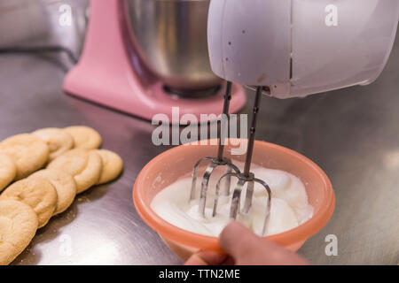 Immagine ritagliata di chef maschio pastella di miscelazione nella ciotola con il mixer a mano sul bancone cucina in laboratorio Foto Stock
