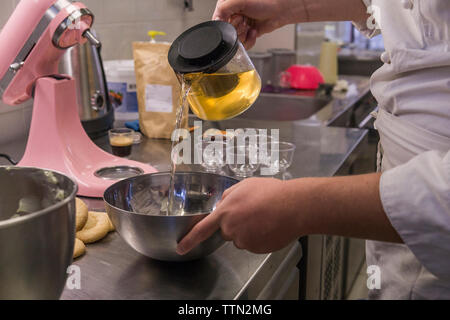 Sezione mediana dei maschi di baker versando acqua nel recipiente di miscelazione sul bancone cucina in laboratorio Foto Stock