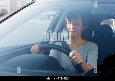 Donna matura la guida auto visto attraverso il parabrezza Foto Stock