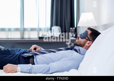 Vista laterale di imprenditore che indossa la maschera per gli occhi mentre dorme nella camera di albergo Foto Stock