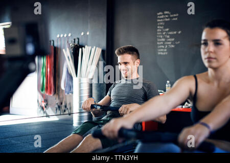 Felice l'uomo esercita sulla macchina di canottaggio in palestra Foto Stock